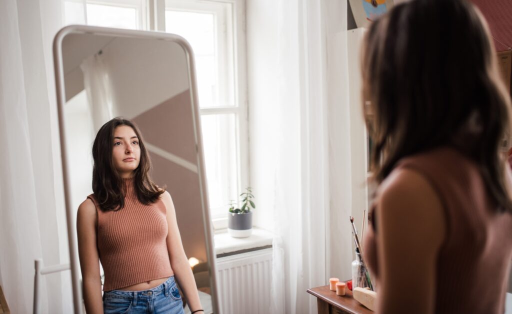 Young teenage girl looking in the mirror in the room.
